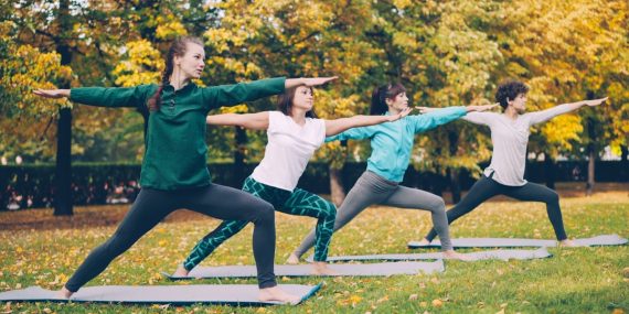 Yoga class is doing stretching exercises in park enjoying autumn nature, fresh air and physical activity. Well-being, recreation and sporty young people concept.